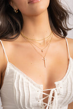 Model wearing elegant gold layering necklaces featuring a dainty thin twist chain, pendant necklaces, and a gold cross pendant necklace. 