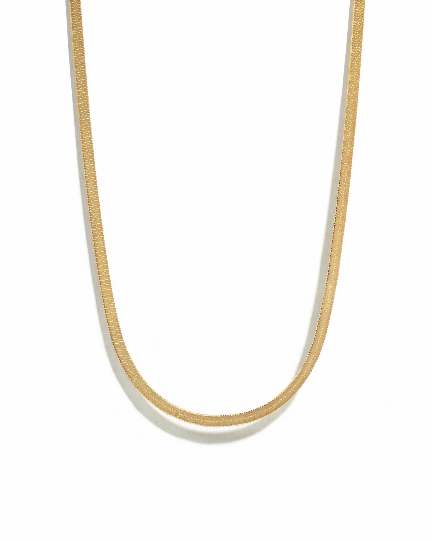 Gold herringbone chain necklace on white background.