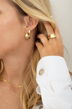 Model wearing statement gold ring with chunky basket hoops and pave huggies