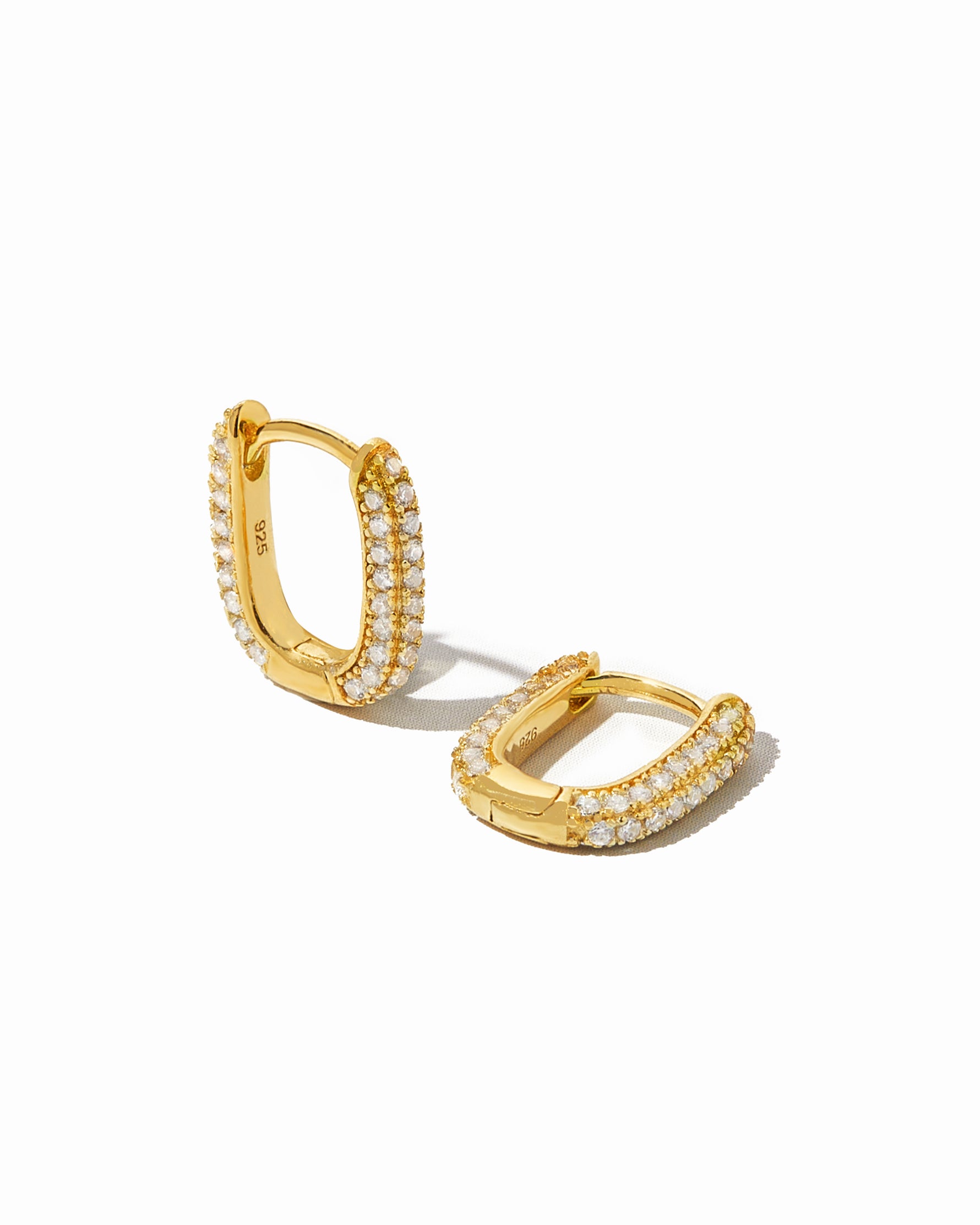 Pavé dainty gold oval huggie earrings on white background.