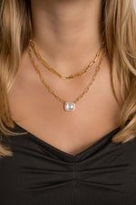 Model wearing two gold paperclip necklaces featuring a statement square paperclip necklace and a baguette pendant necklace. 