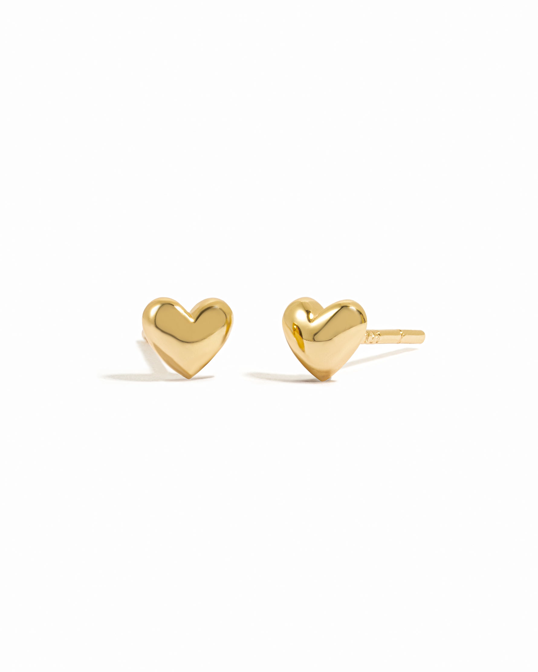 Sleek small gold heart stud earrings on white background