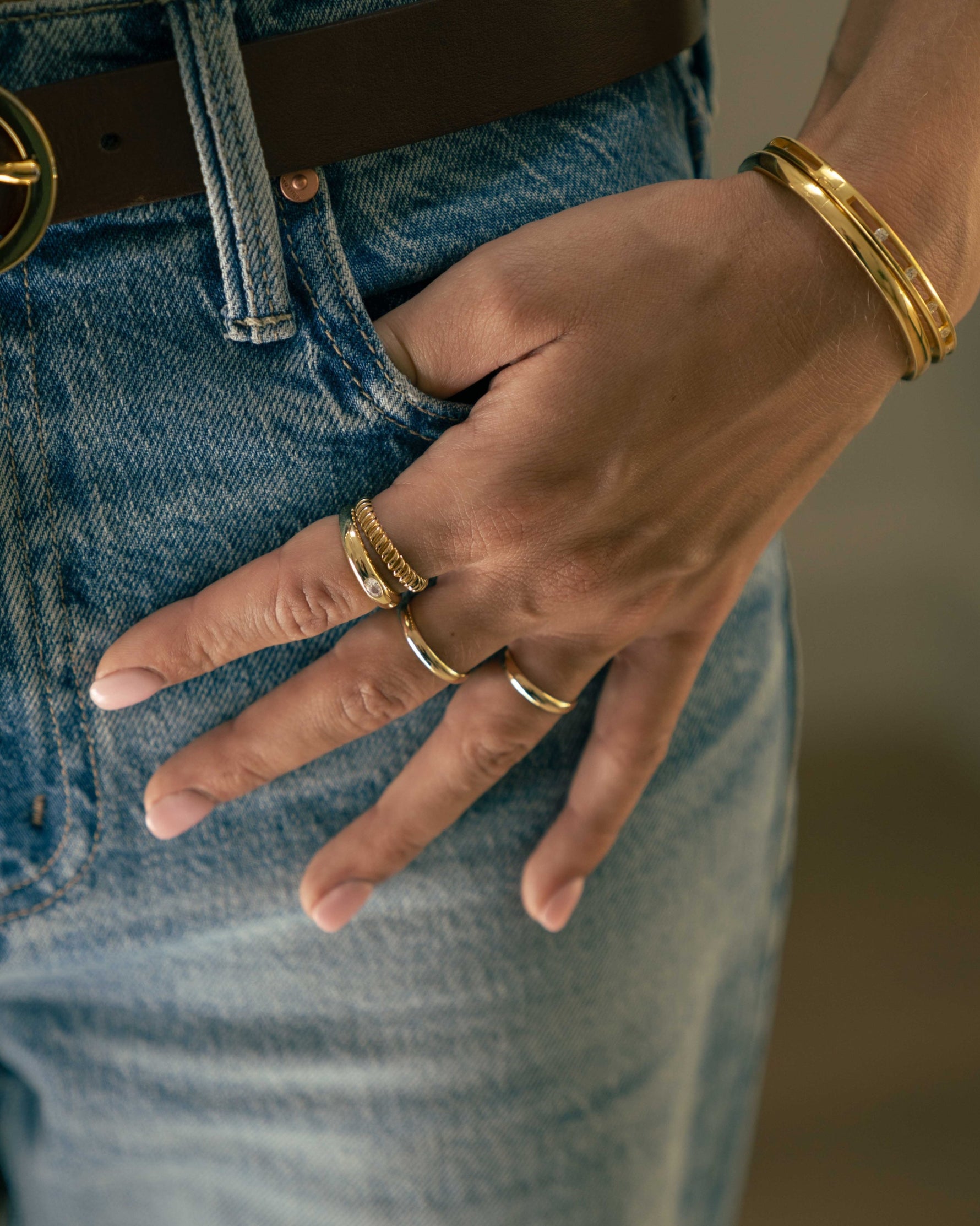 Model wearing sleek gold jewelry featuring two gold bangles and gold stacking rings. 