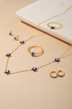Gold sapphire gemstone jewelry look including sapphire flower earrings, sapphire marquise and baguette rings, and sapphire huggie earrings.
