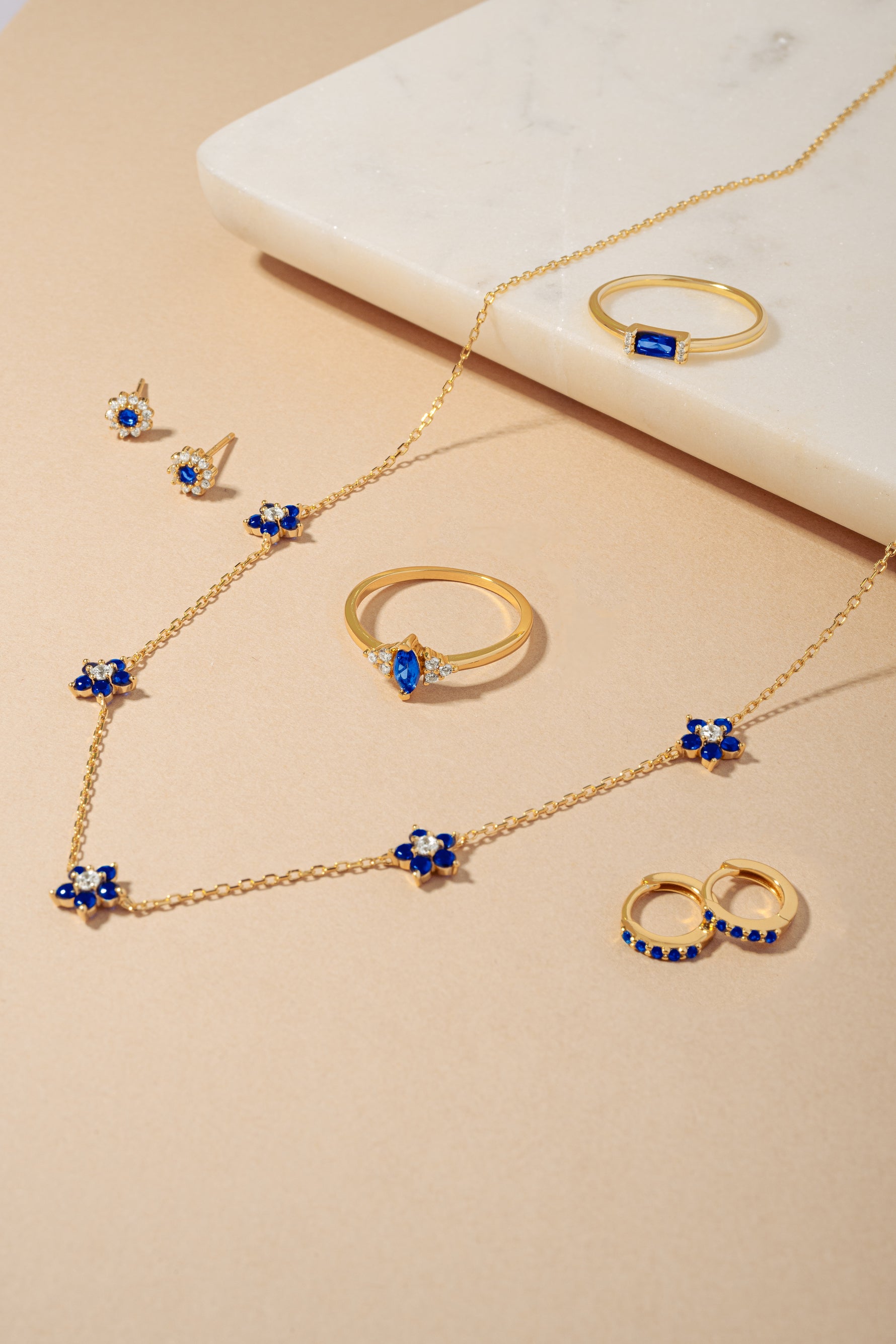 Gold sapphire gemstone jewelry look including sapphire flower earrings, sapphire marquise and baguette rings, and sapphire huggie earrings.