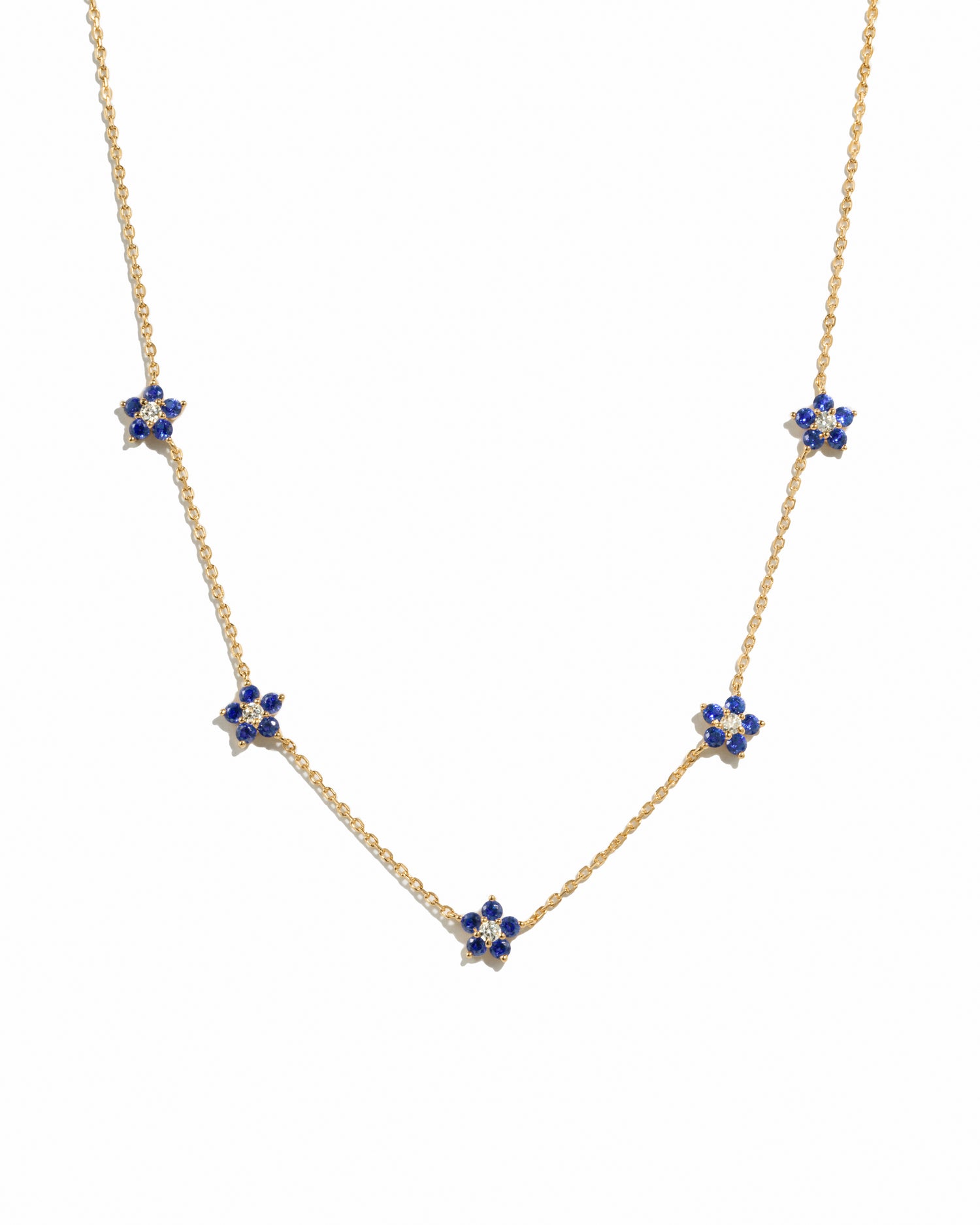 Minimalist gold sapphire flower charm necklace on white background