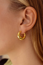 Model wearing chunky gold basket hoops solo.