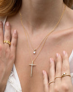 Model wearing cushion diamond gold necklace and large cross pendant necklace. 