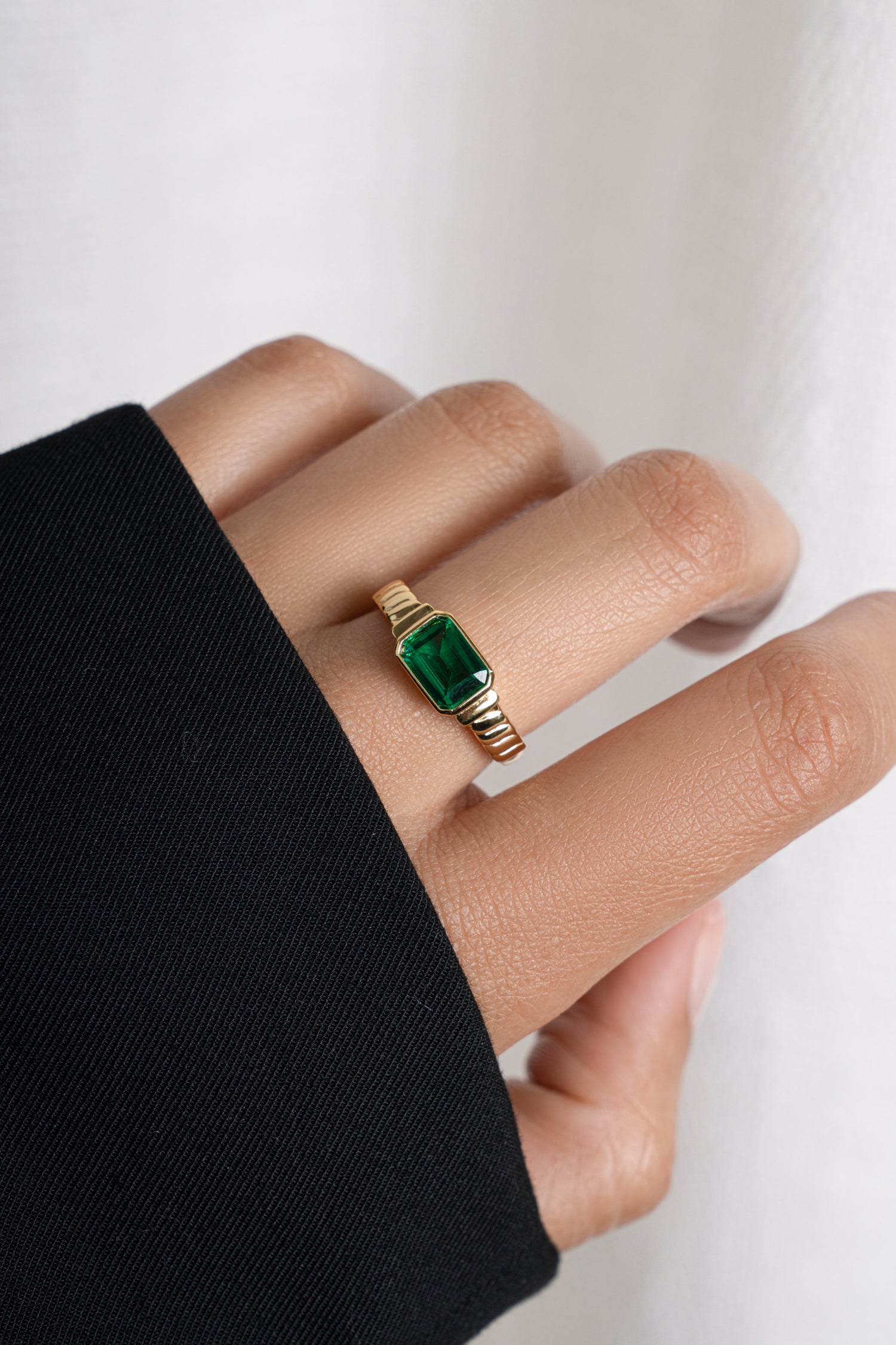 Model wearing gold emerald statement ring with textured band. 