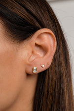 Model wearing gold emerald cut stud earrings paired with 3 stone tiny stud earrings and gold ball stud earrings.