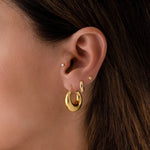 Model wearing sleek everyday honey gold chunky hoop earrings in a stack with minimalist gold huggie earrings and a simple ball stud.