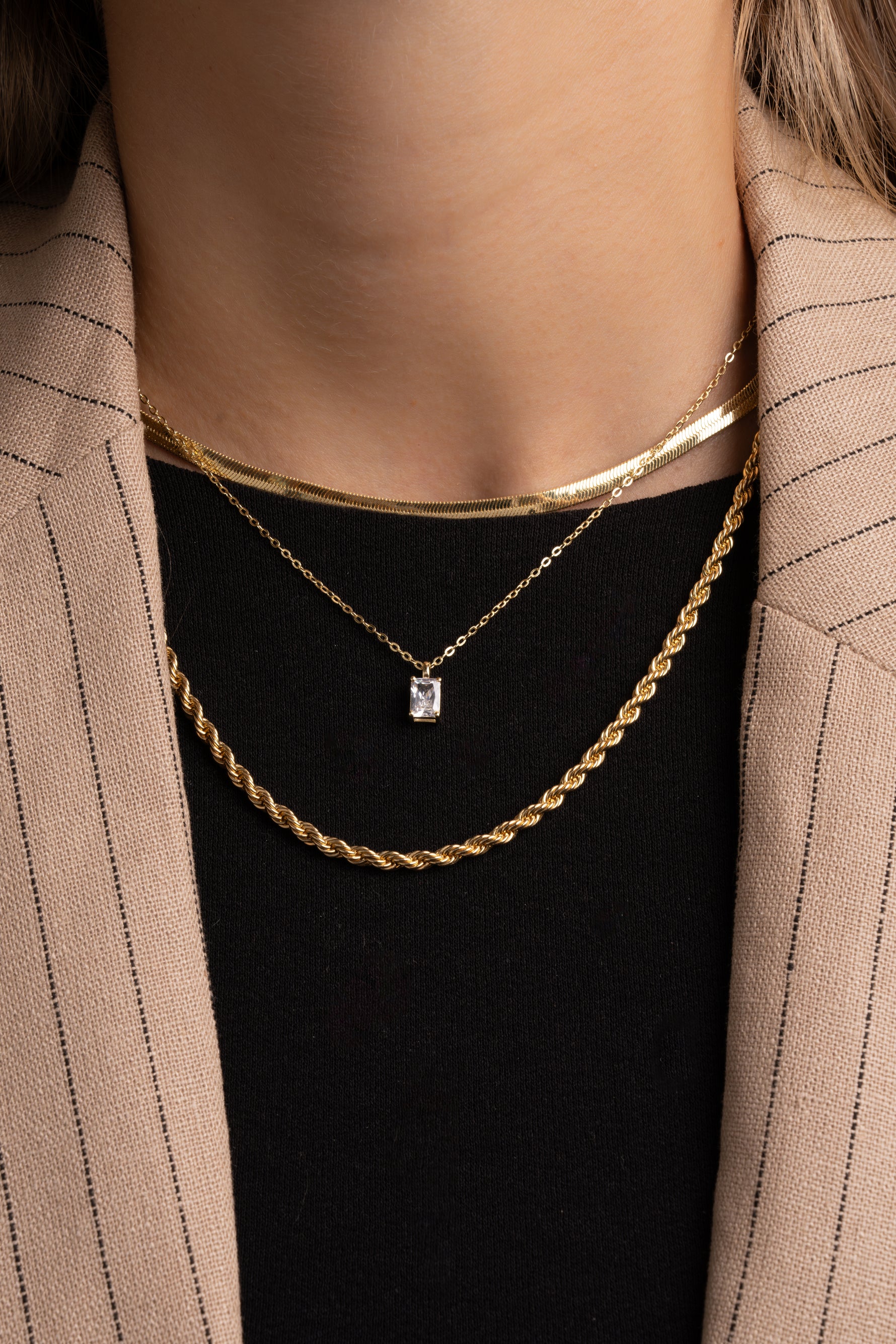 Model wearing herringbone chain necklace, diamond pendant necklace, and chunky rope chain necklace.