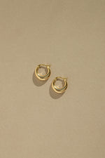 Dainty gold huggie hoop earrings on tan paper. 