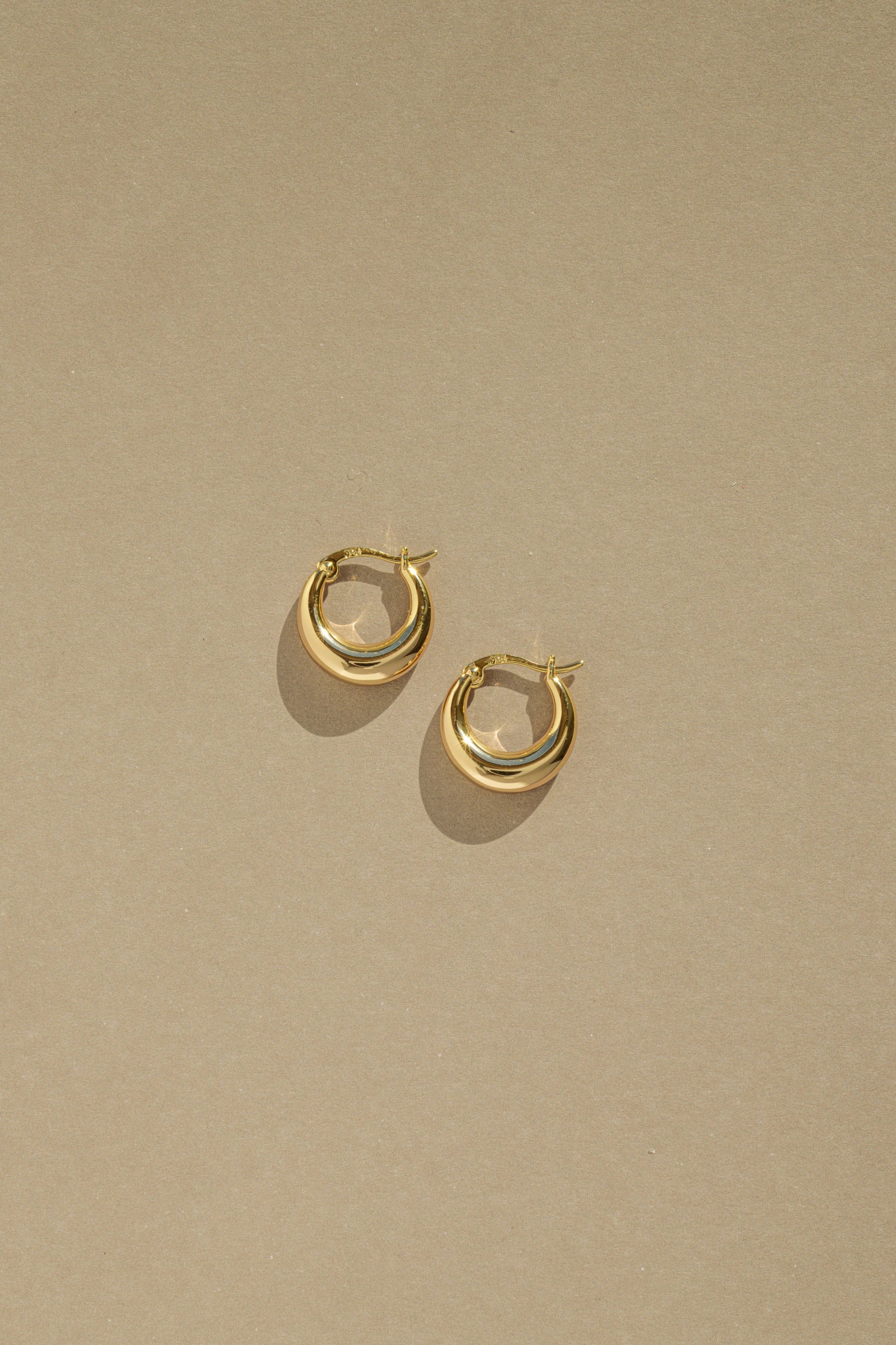 Dainty gold huggie hoop earrings on tan paper. 
