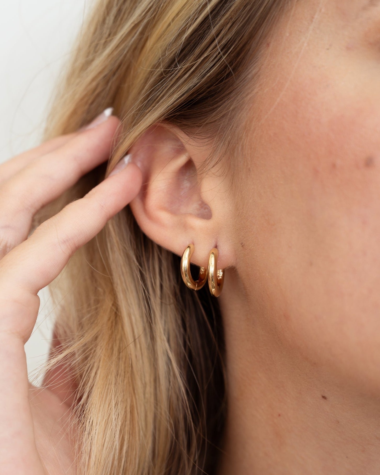 Model wearing two gold minimalist hoop earrings