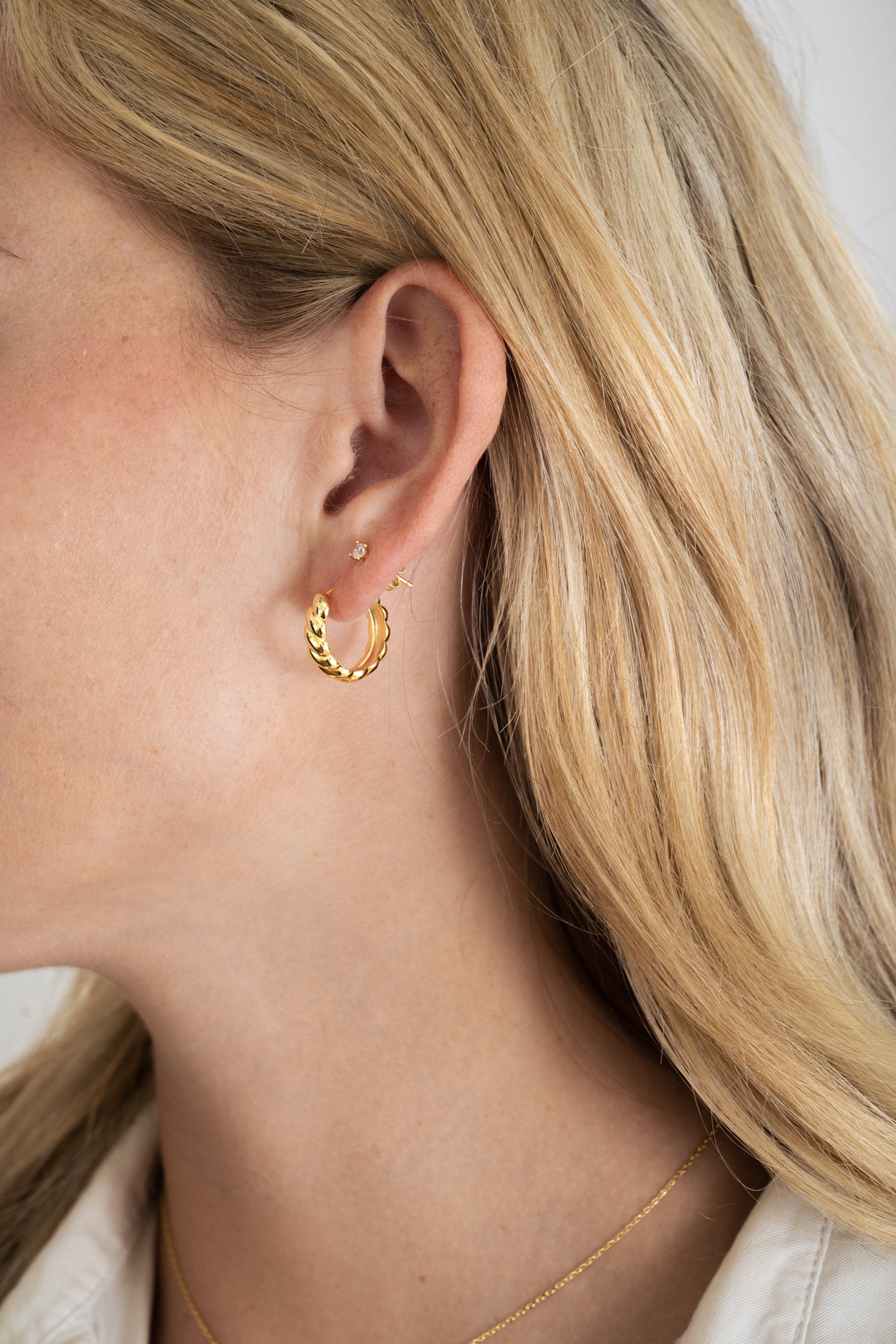 Model wearing gold texture croissant hoops with solitaire stud diamond earrings. 