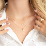 Model wearing minimalist and trendy gold necklaces in a stack featuring a heart pendant, a butterfly pendant, and a cushion diamond necklace. 