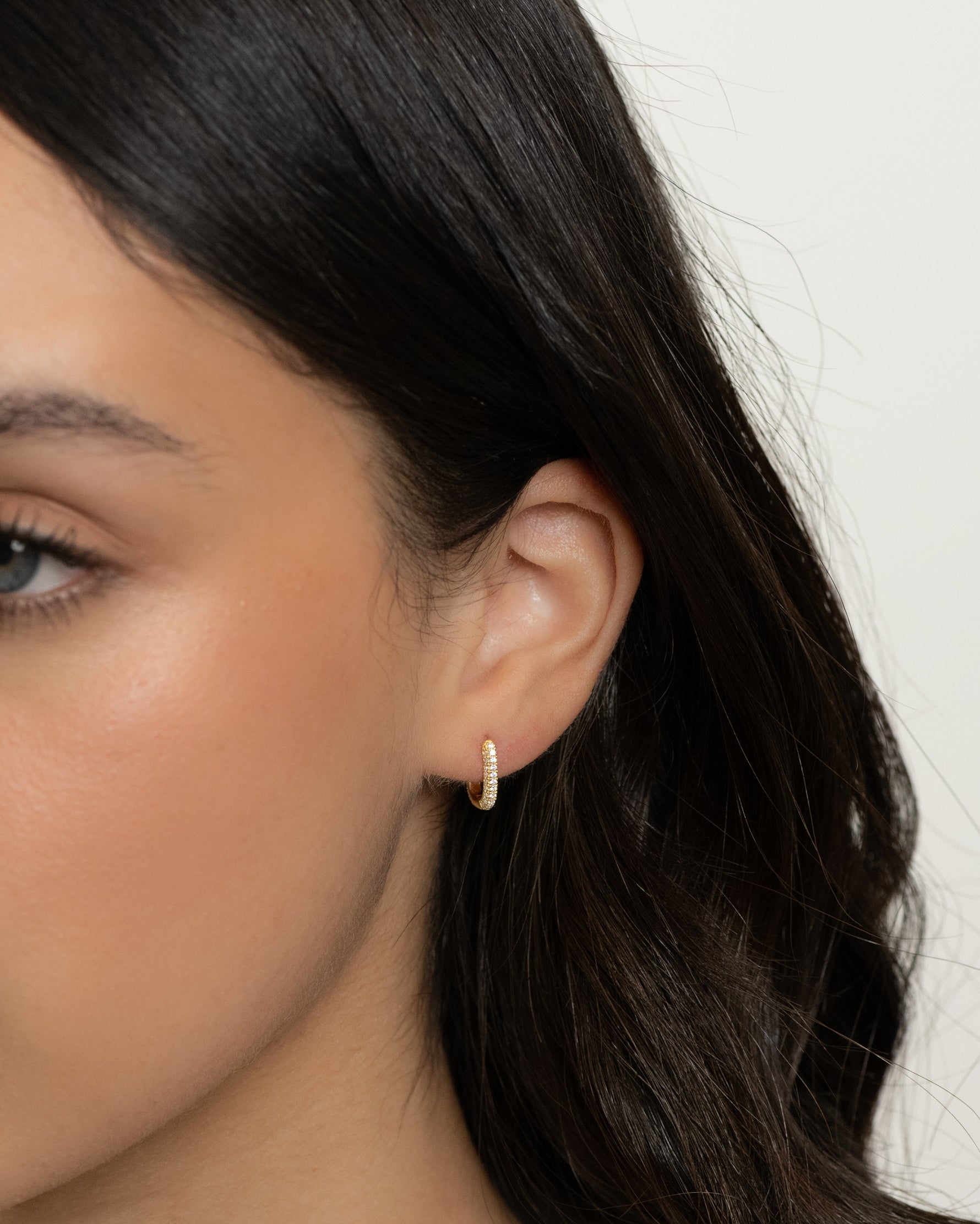 Model wearing gold studded square hoop earrings with pavé design. 