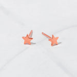 Rose gold stud star earrings on marble background.