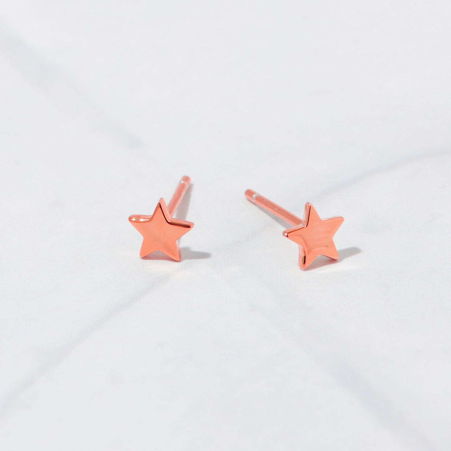 Rose gold stud star earrings on marble background.