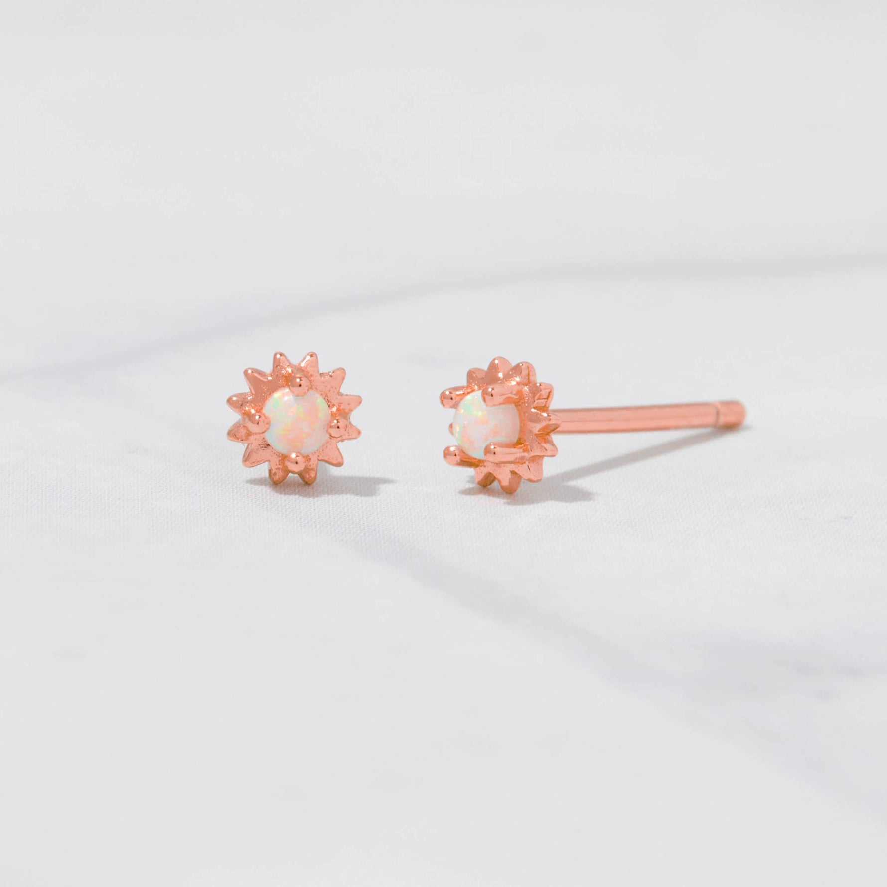 Upclose shot of rose gold dainty sunburst stud earrings with opal center.  
