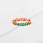 Rose gold emerald slanted eternity ring on marble background. 