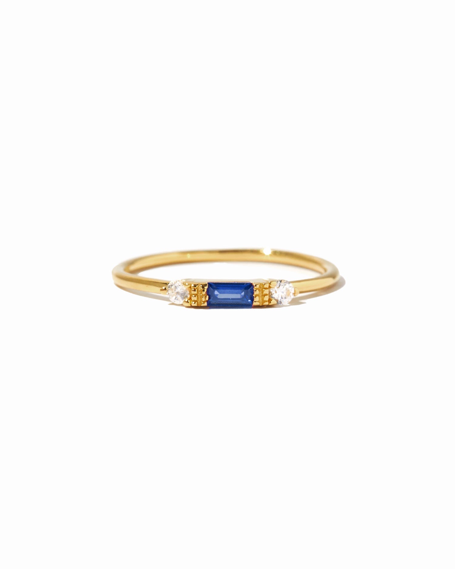 Dainty gold sapphire birthstone stacking baguette ring on white background.
