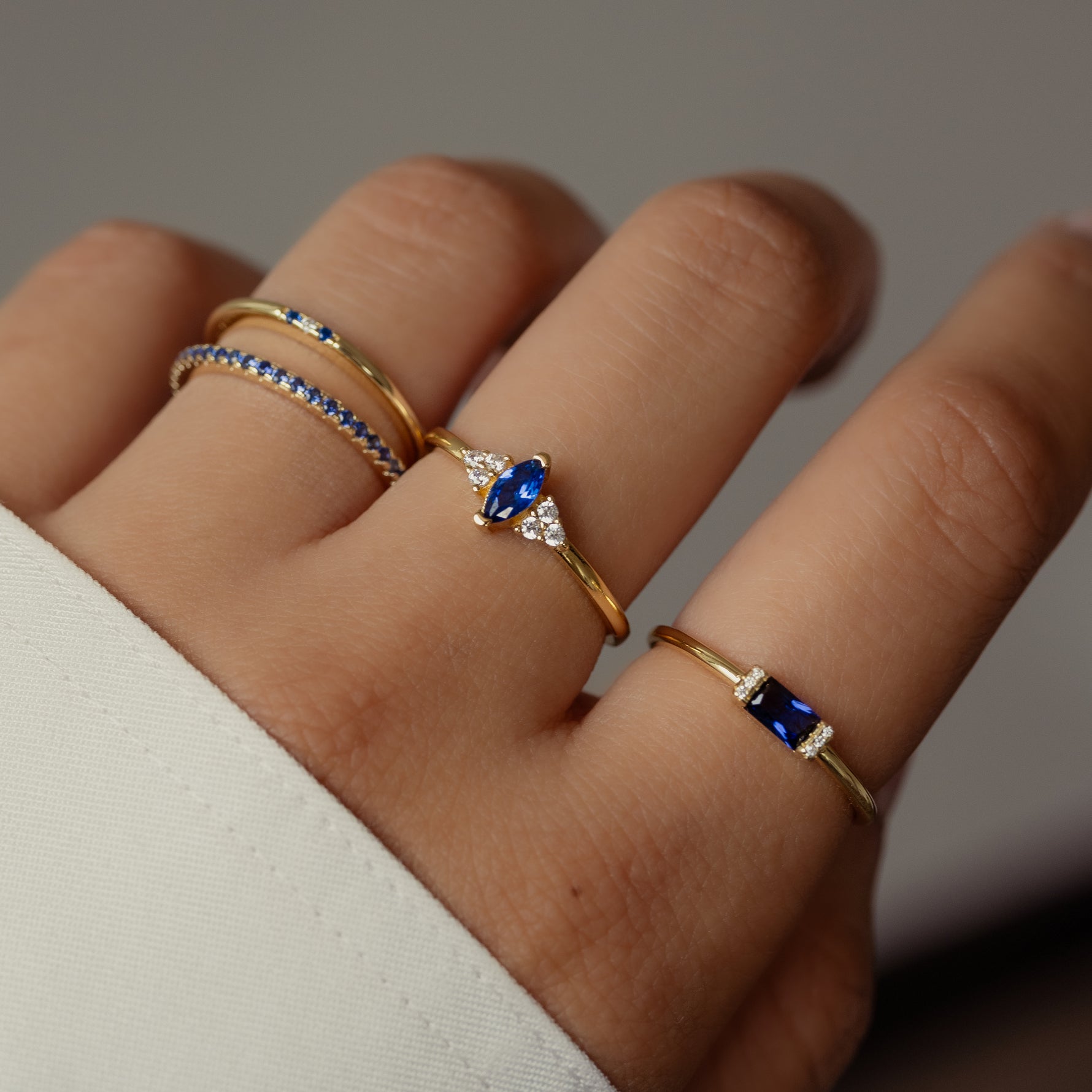 Model wearing trendy gold sapphire gemstone ring stack. 