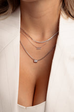 Model wearing sterling silver trendy necklaces in a stack featuring a half cz tennis half paperclip necklace, an angel number necklace, and a dainty baguette bezel pendant necklace. 