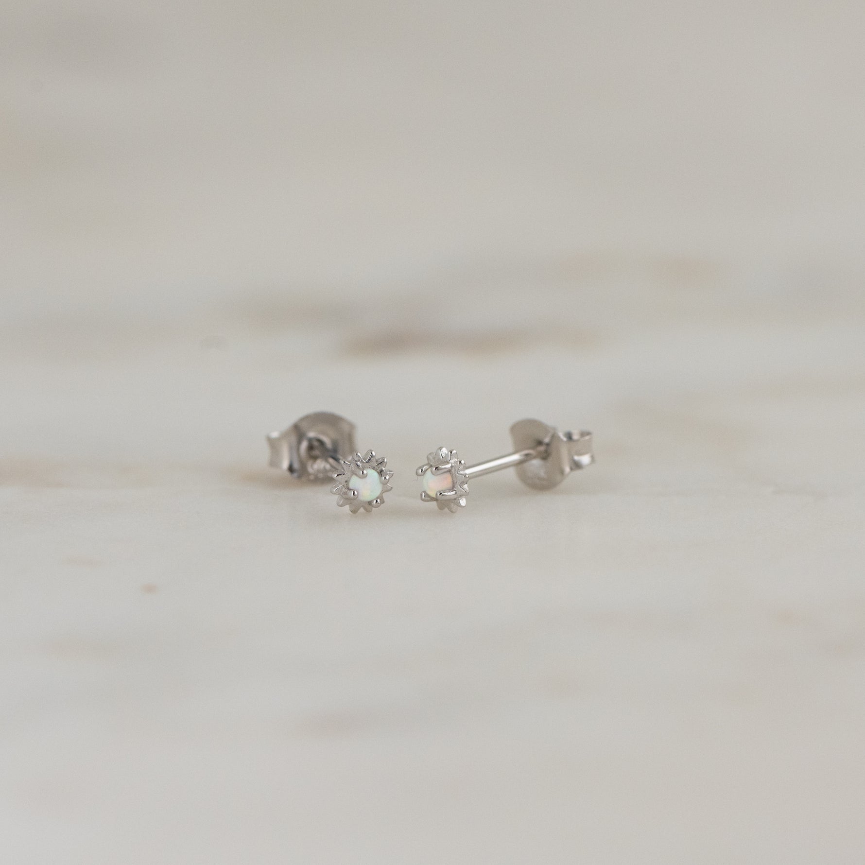Tiny sterling silver opal vibrant stud earrings on marble background.