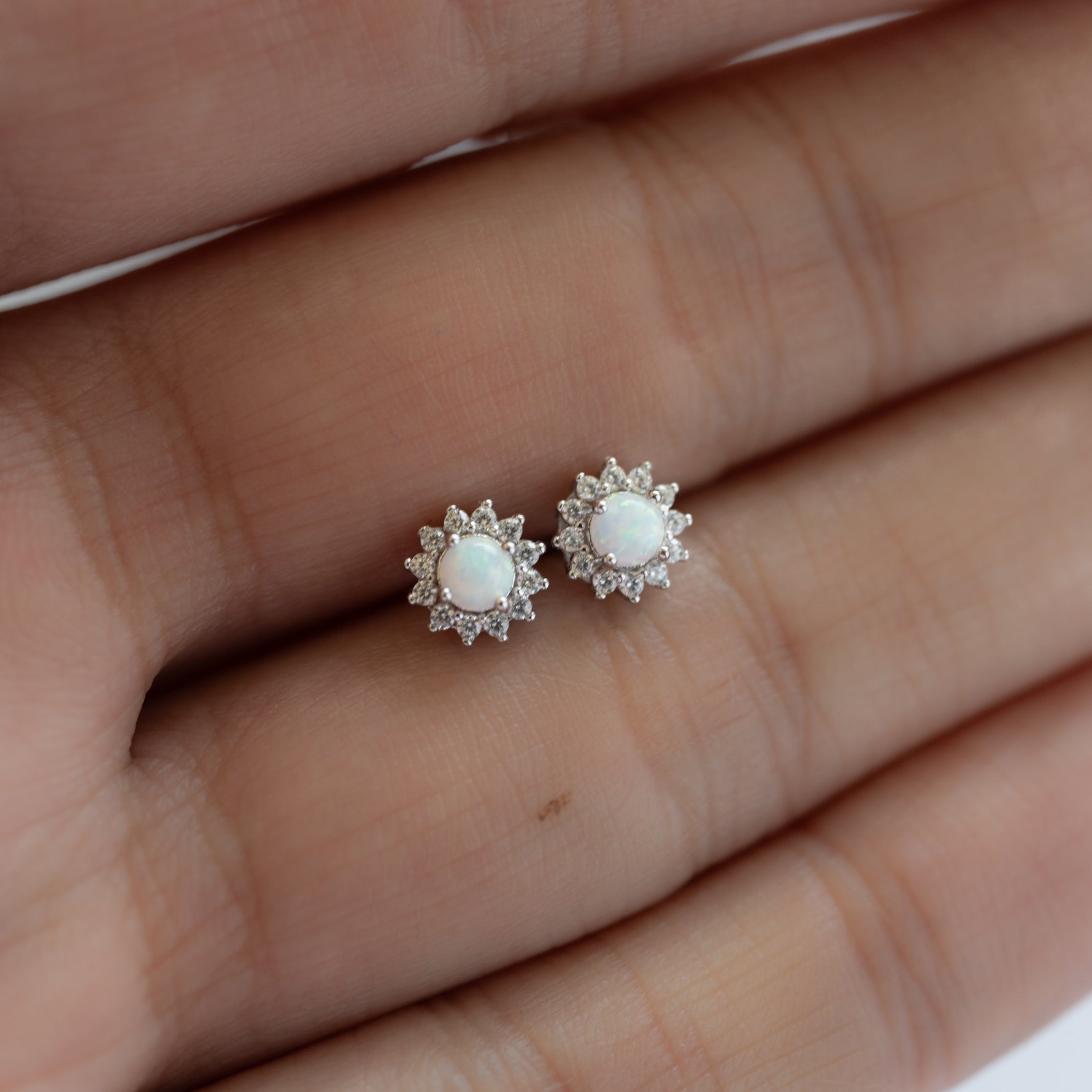 Model holding delicate opal and cz stud earrings in silver. 