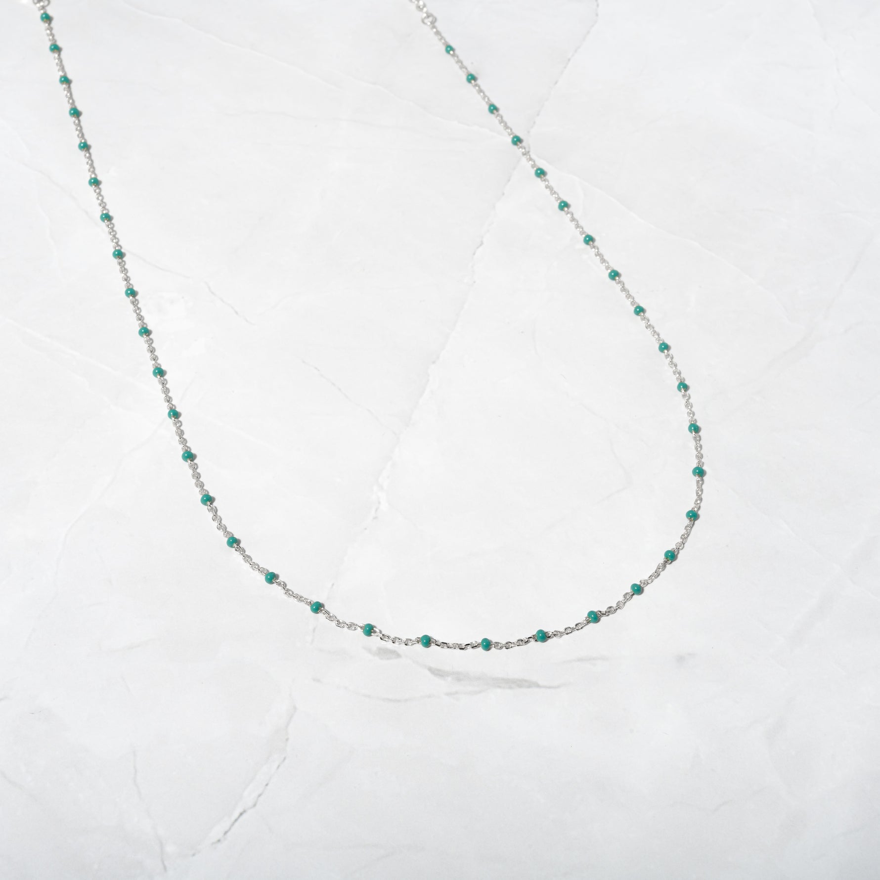 Silver delicate turquoise enamel beaded necklace on marble background.