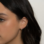Model wearing delicate gold studded oval hoop earrings. 