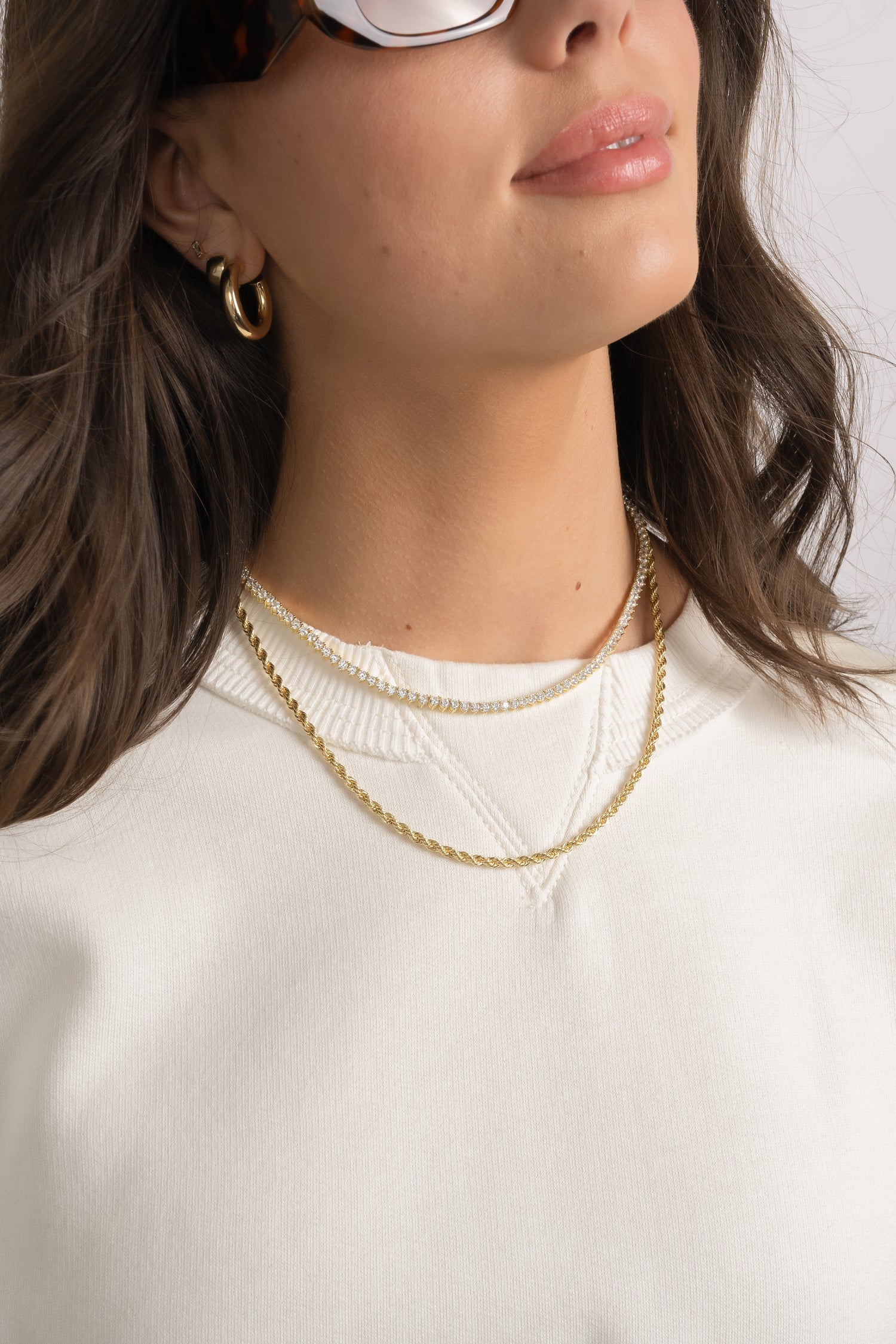 Model wearing diamond tennis necklace and gold rope chain necklace.
