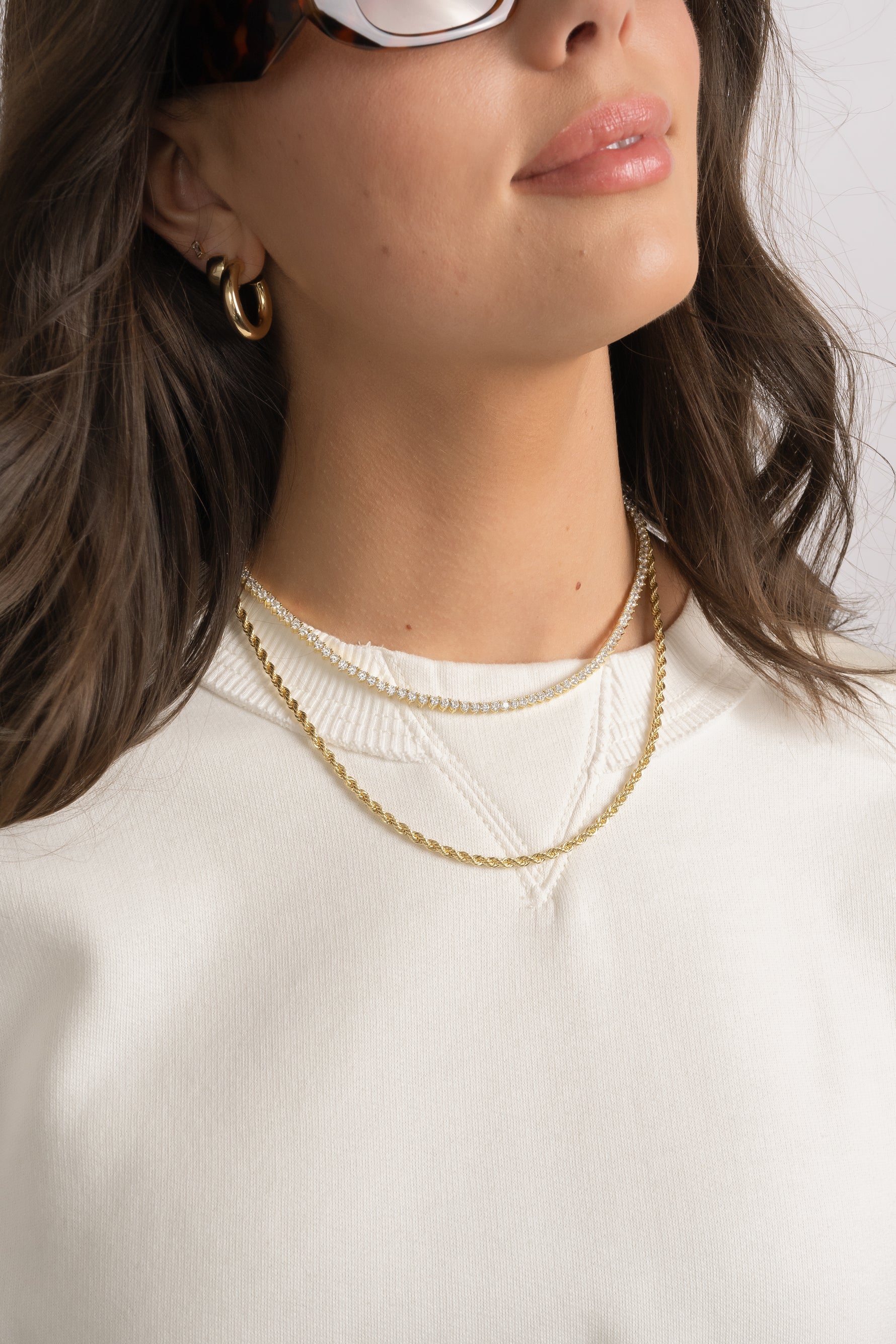 Model wearing diamond tennis necklace and gold rope chain necklace.