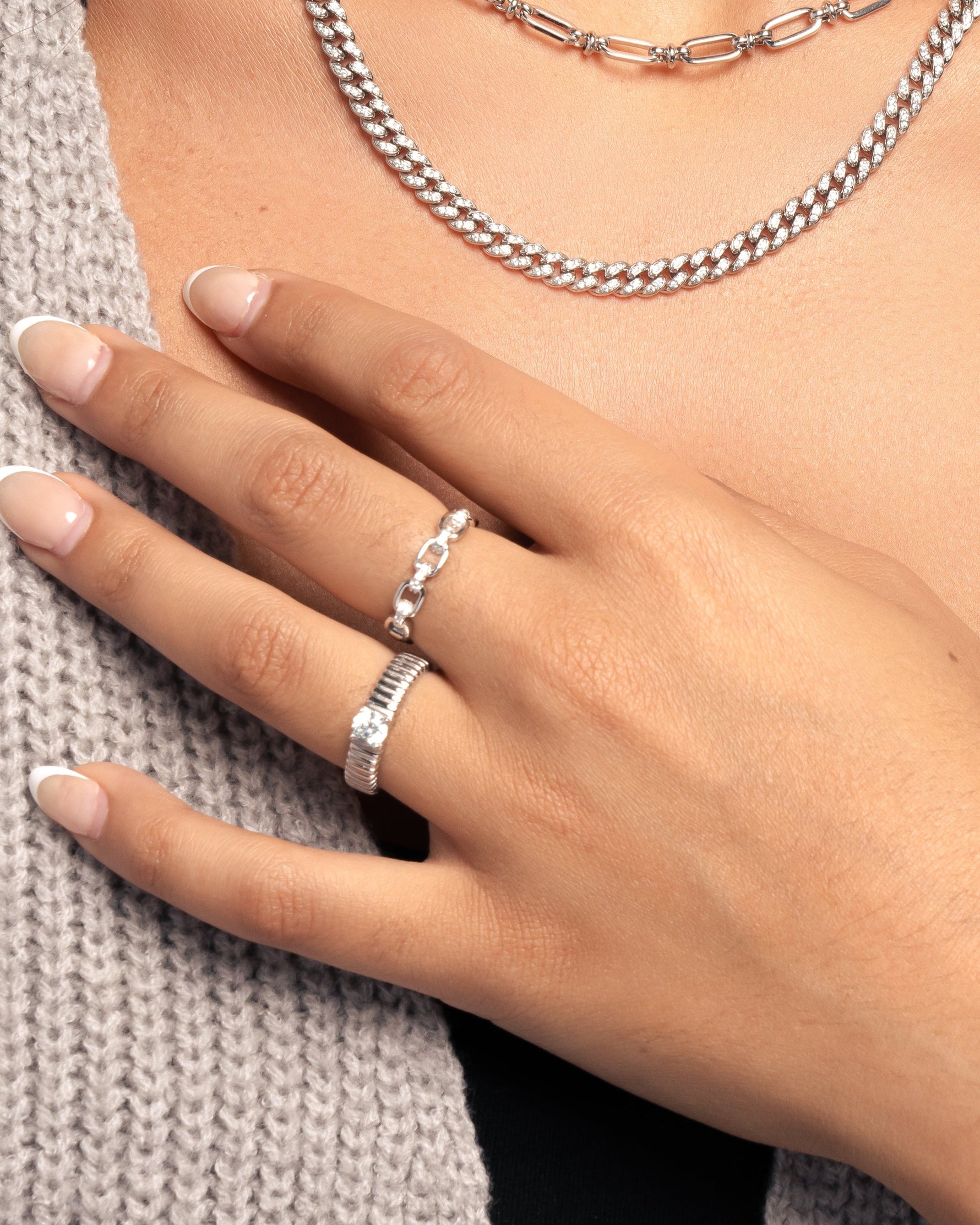 Model wearing sterling silver trendy jewelry look featuring a chain link ring and fluted solitaire ring, paired with a pavé curb link chain necklace. 