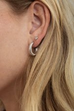 Model wearing textured ribbed silver hoops with silver heart studs.