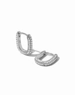 Pavé dainty sterling silver oval huggie earrings on white background.