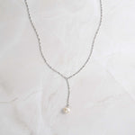 Pearl lariat with silver chain on marble background.