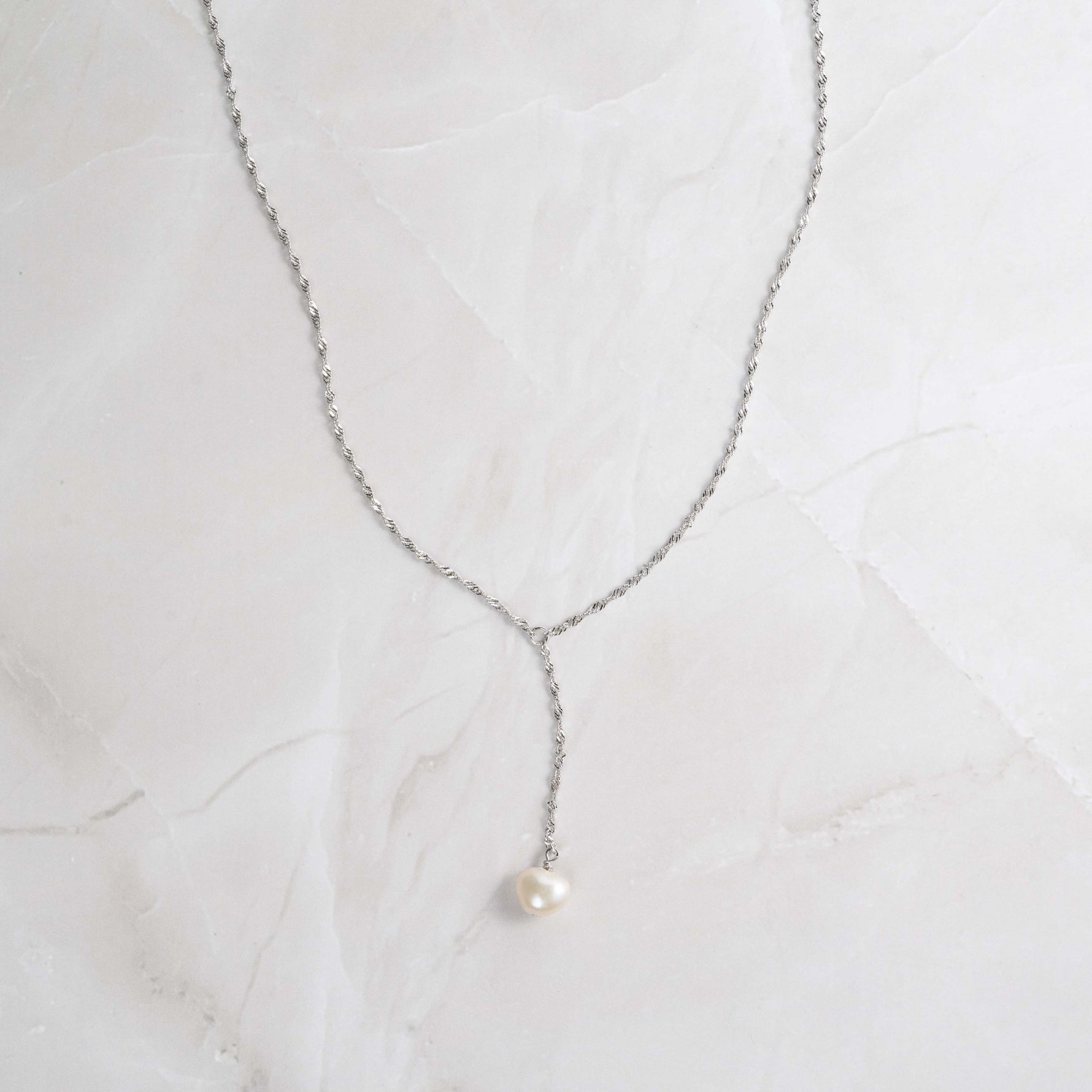 Pearl lariat with silver chain on marble background.
