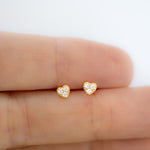Model holding tiny diamond gold heart stud earrings. 