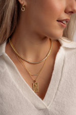 Model wearing three gold layering necklaces.