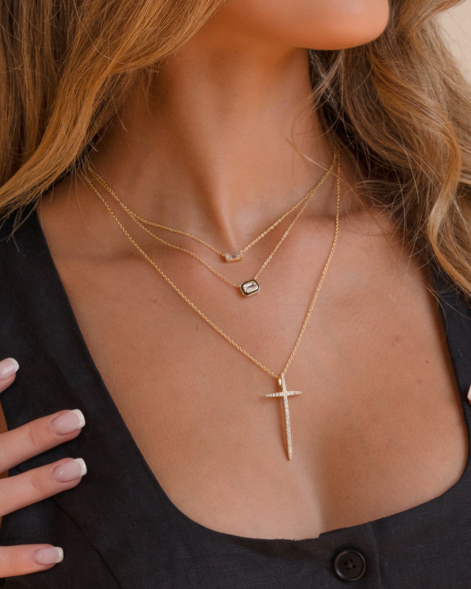 Model wearing baguette pendant necklace, black enamel baguette necklace, and large gold cross pendant necklace. 