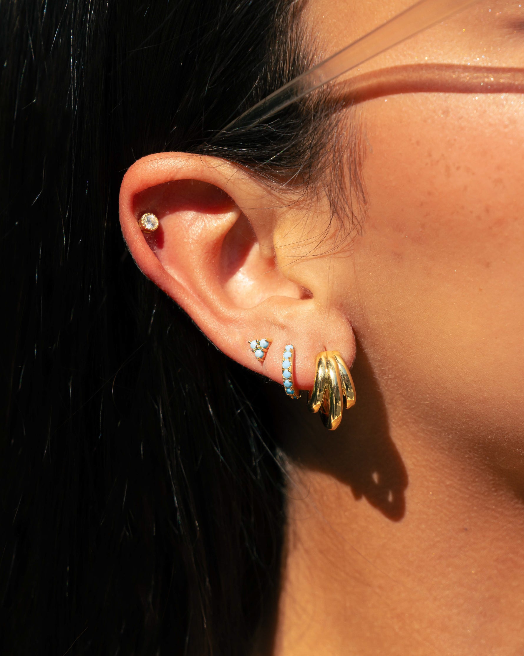 Model wearing multiple gold and turquoise earrings on ear.