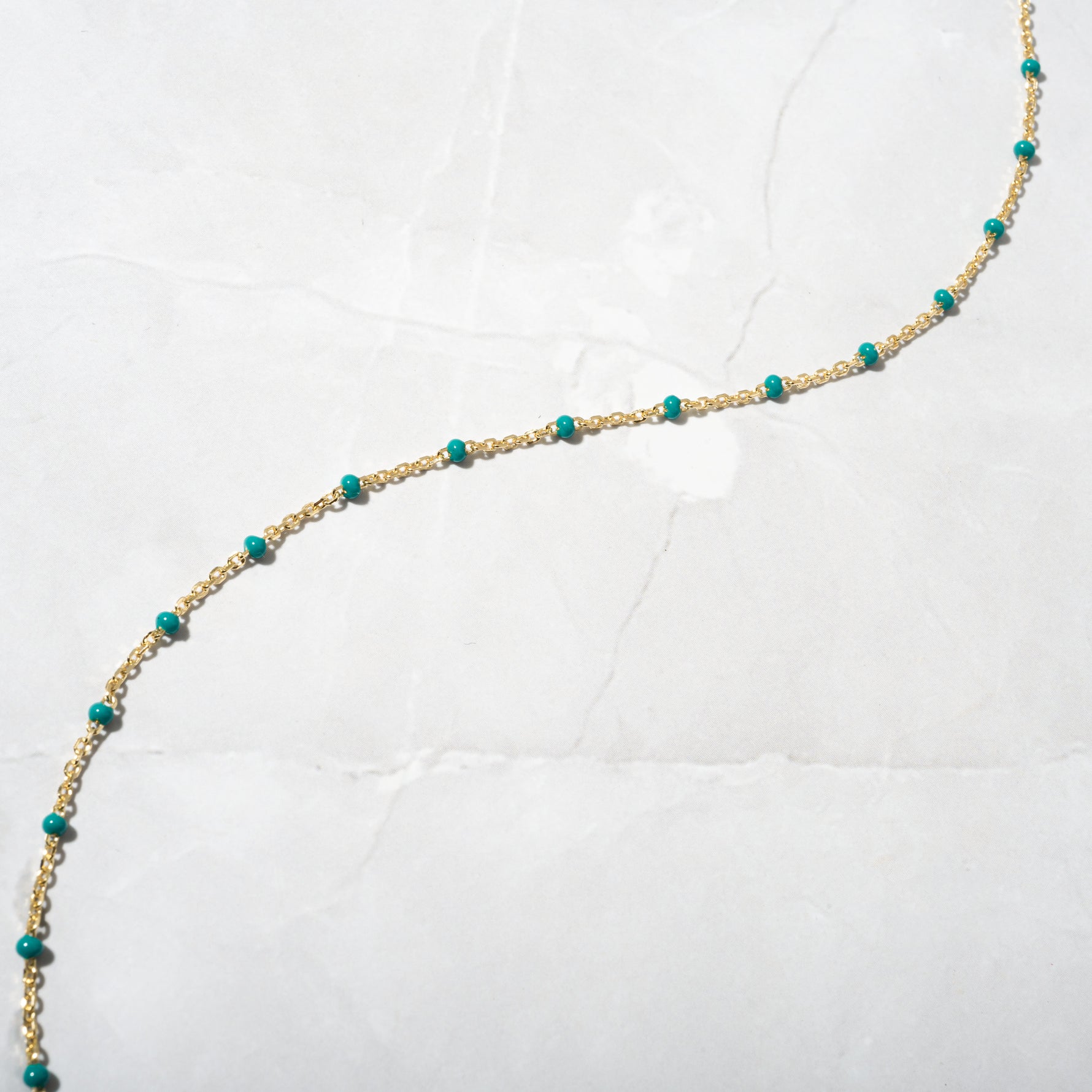 Minimalist gold beaded turquoise necklace on marble background. 