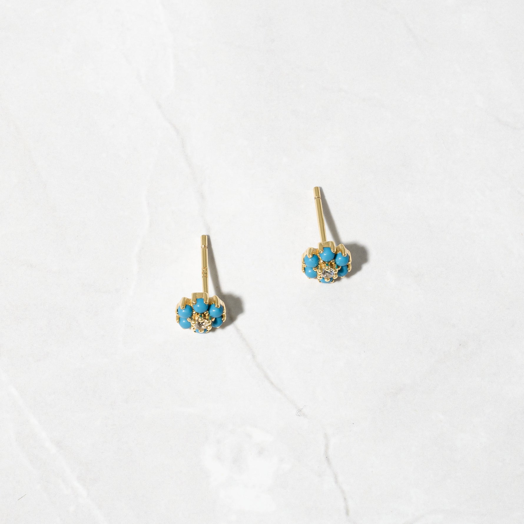 Gold flower stud earrings on marble background. 