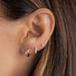 A close up of a model with three piercings, a small gold hoop earrings with an aquamarine gemstone strip in the center, a small pave huggie hoop, and a diamond stud