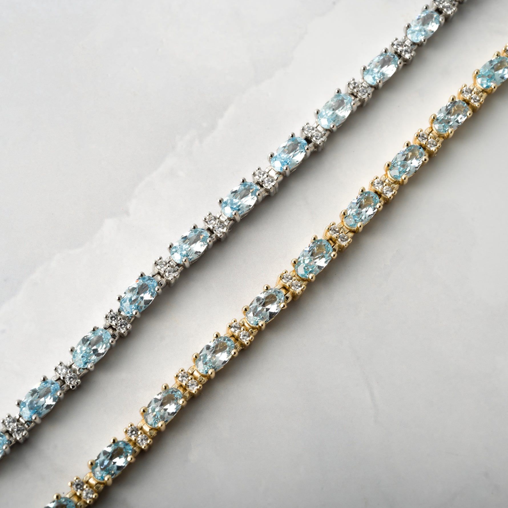 closeup image of gold aquamarine tennis bracelet and silver aquamarine bracelet