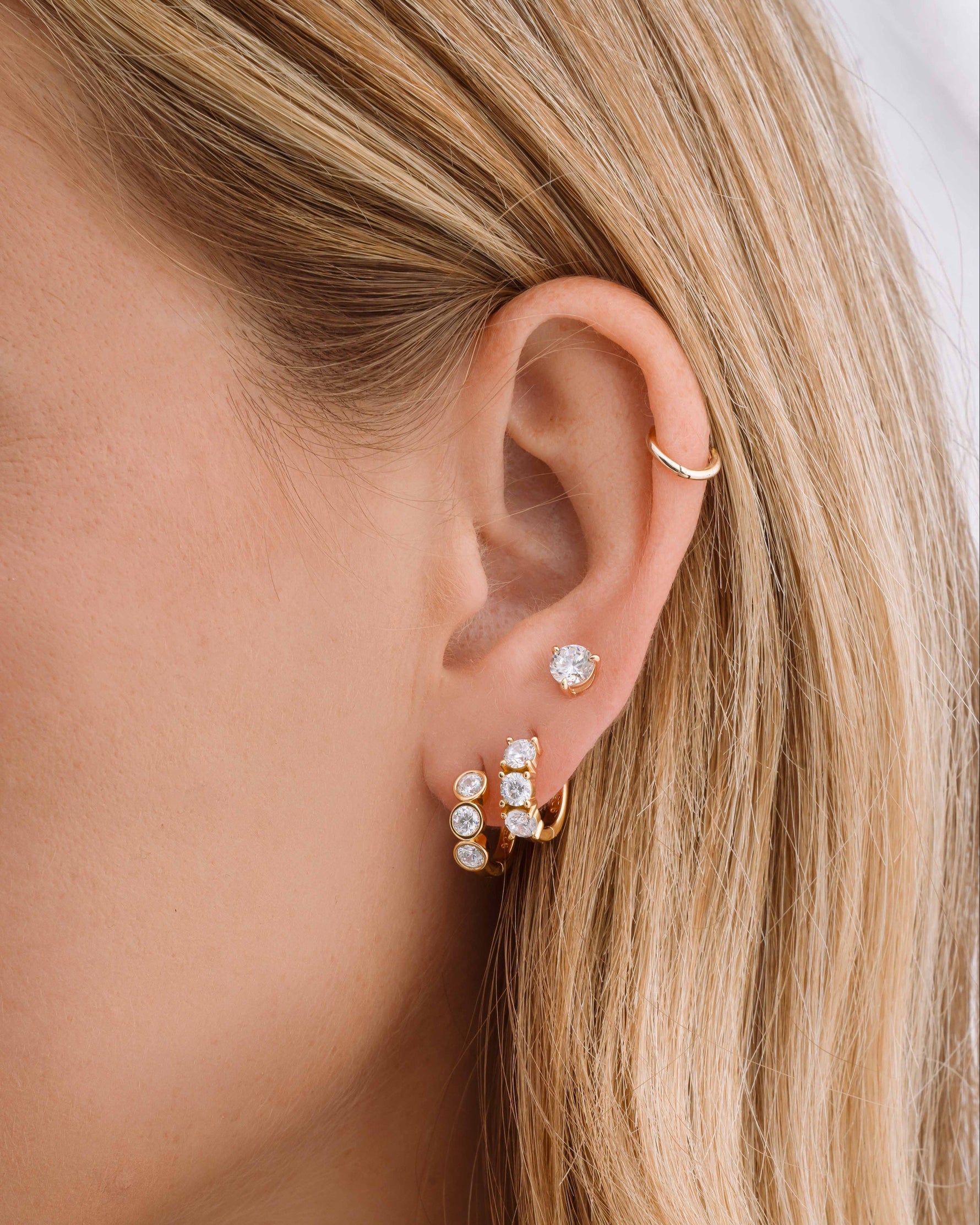 Gold Bezel 3 Stone Huggie Hoop Earrings by Sami Jewels worn on a model's ear, showcasing their stacked design and elegant style.