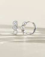 Side view of Sami Jewels Bezel 3 Stone Huggie Hoop Earrings featuring three sparkling stones on small gold hoops.